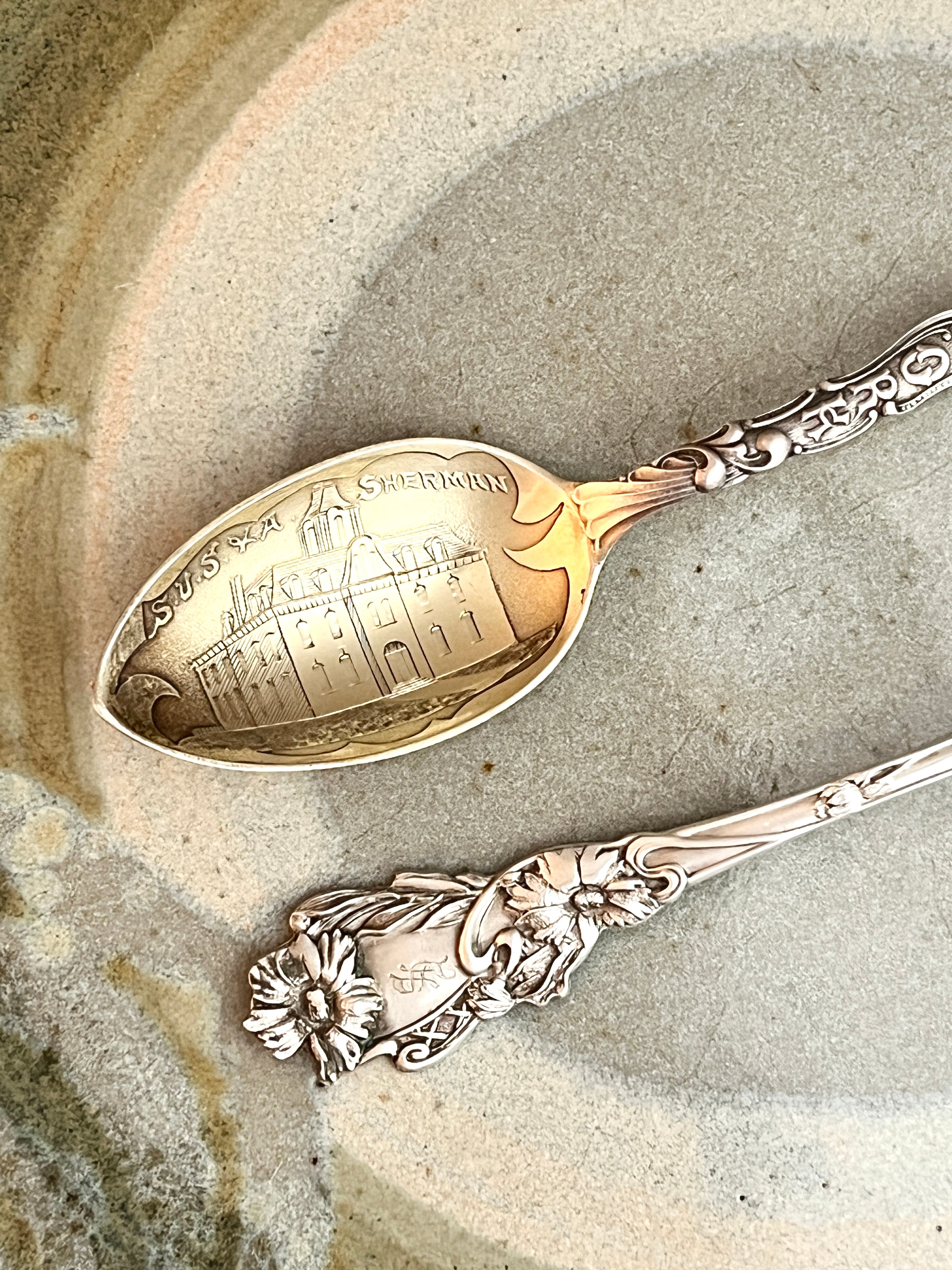 Two ornate spoons with engraved designs on a textured stone surface