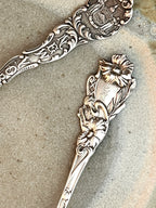 Two ornate sterling silver spoons with floral designs on a textured surface