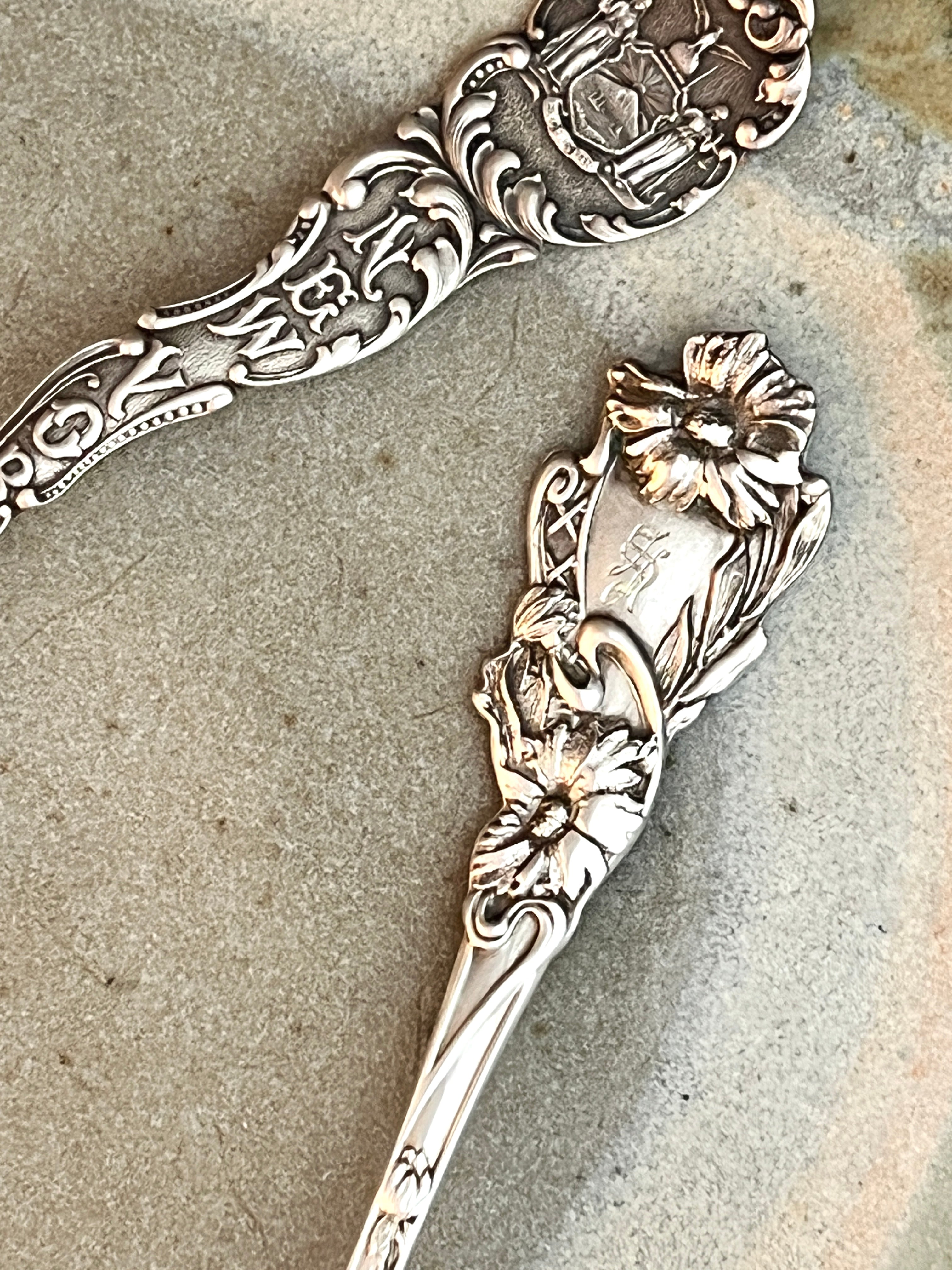 Two ornate sterling silver spoons with floral designs on a textured surface