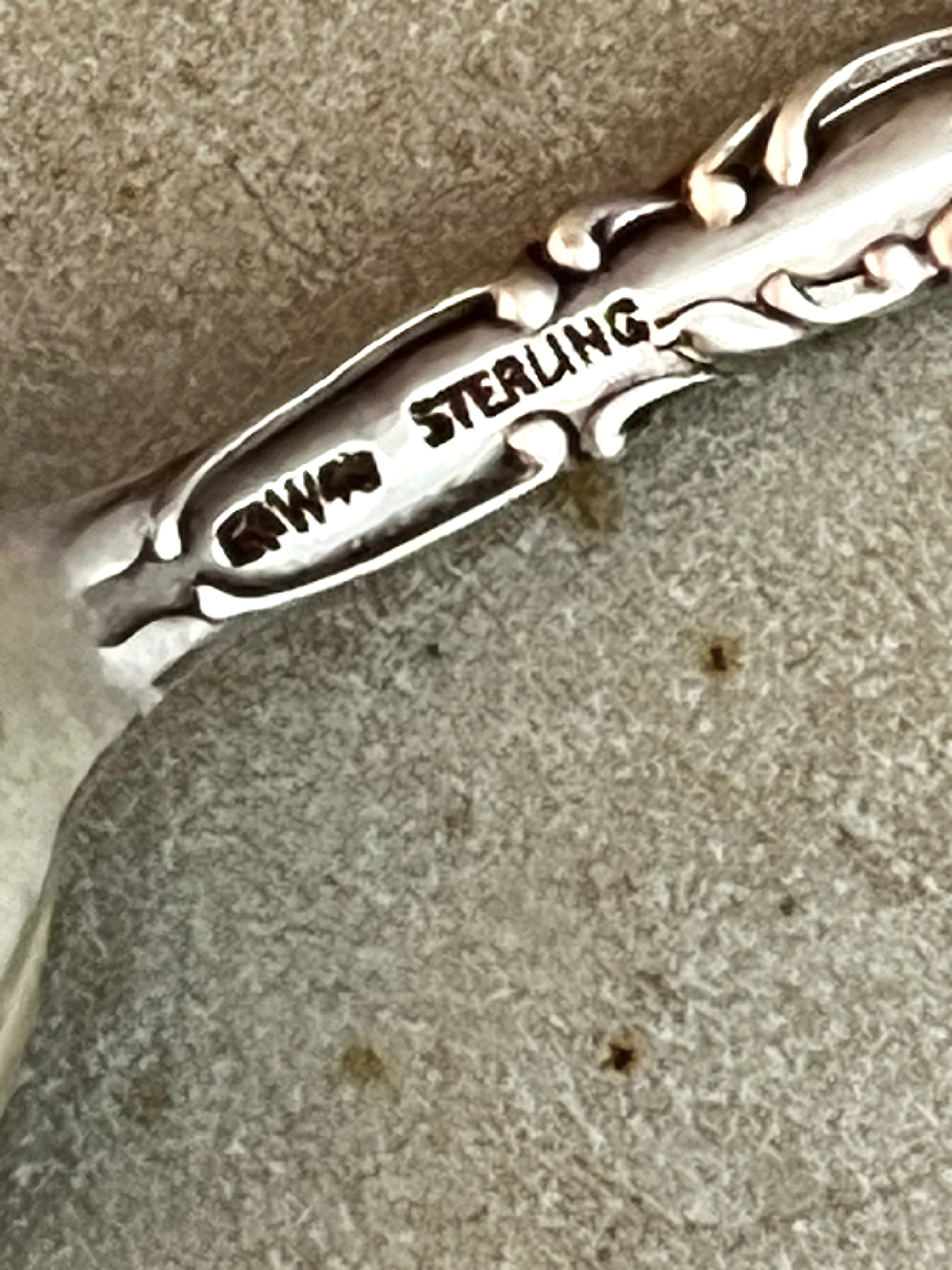Close-up of a silver spoon with 'STERLING' engraved on it, placed on a textured surface.