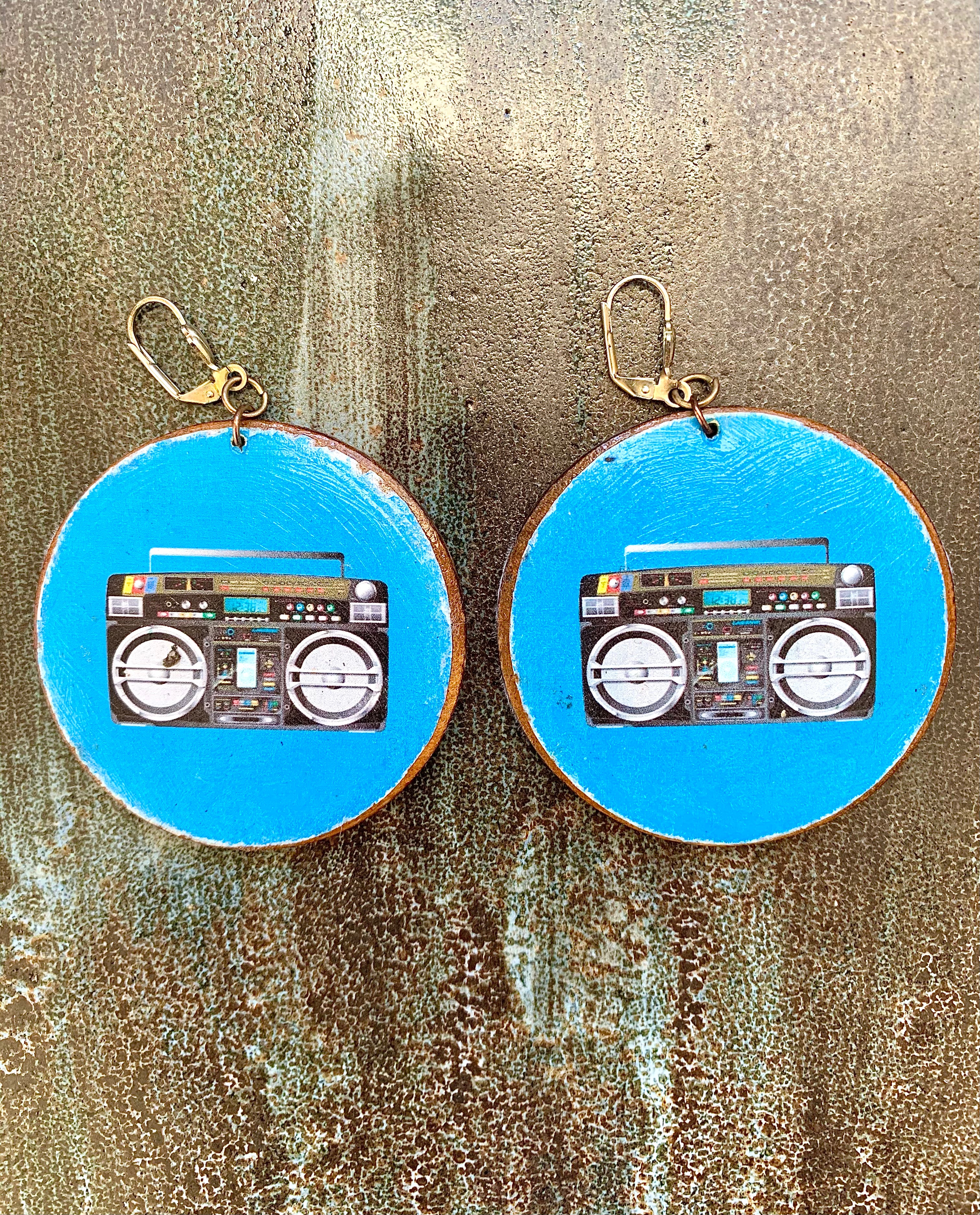 Earrings with a design of a boombox on a blue background, displayed against a textured surface.