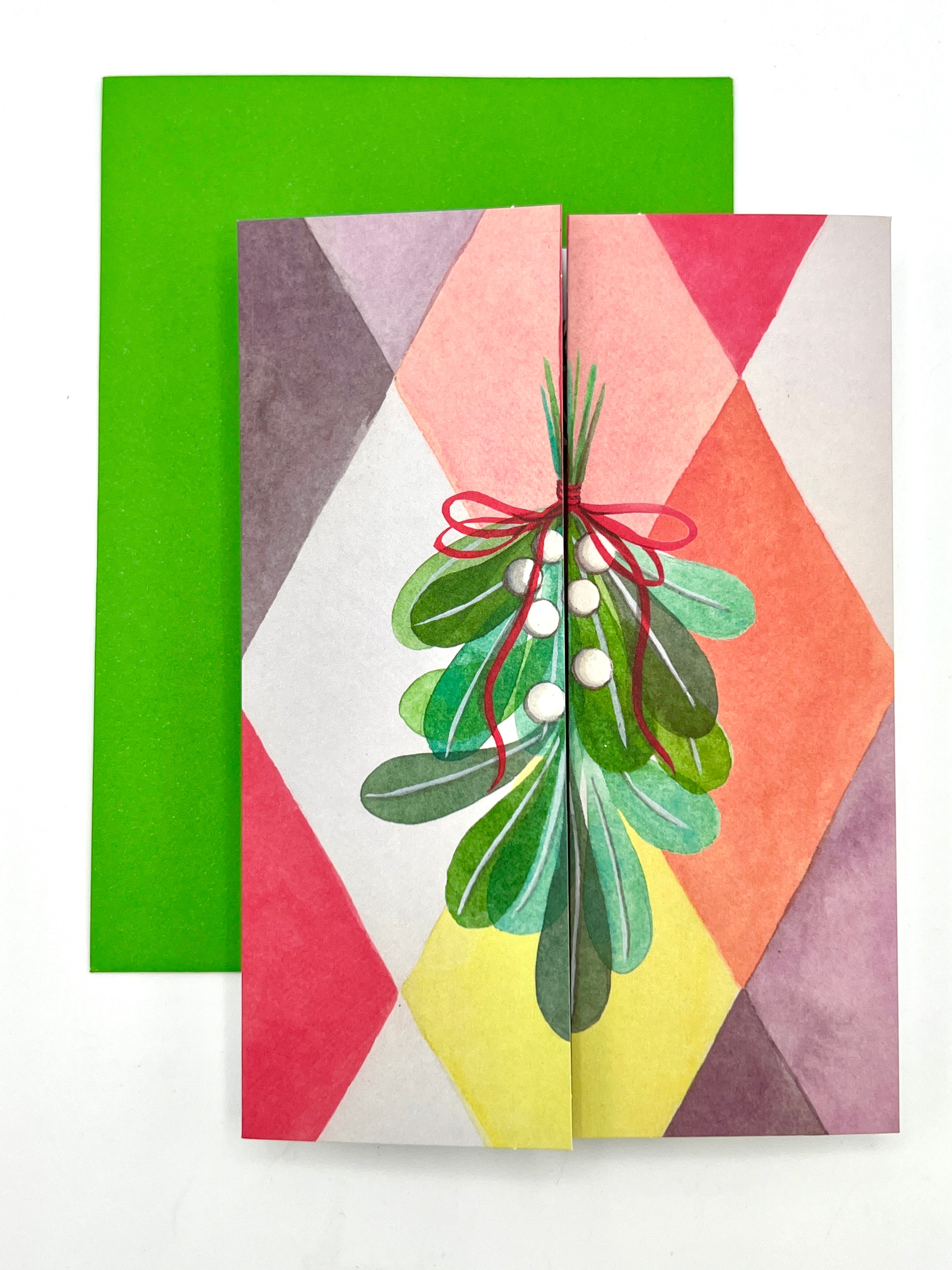 A 3D holiday greeting card with a mistletoe design and red and green leaves, attached to a green envelope.