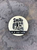 A round pinback button with a black and white design that reads 'SALUTO BE OF GOOD CHEER'.