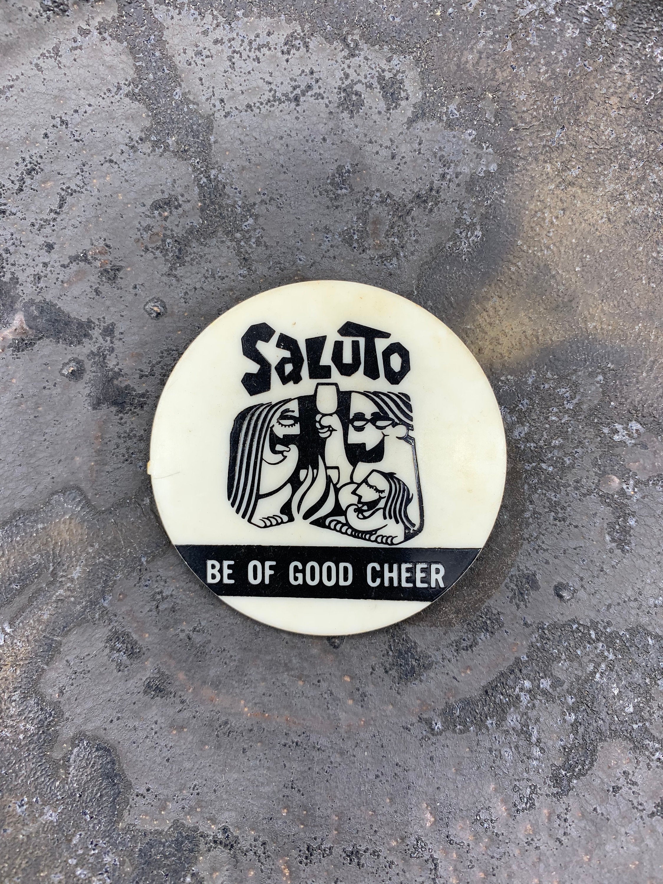 A round pinback button with a black and white design that reads 'SALUTO BE OF GOOD CHEER'.